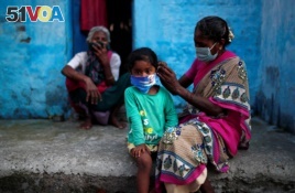 A woman wearing a protective face mask adjusts her daughter's face mask outside their house at a slum area, during an extended nationwide lockdown to slow the spreading of the coronavirus disease (COVID-19), in New Delhi, India, June 24, 2020