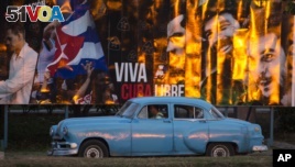 A taxi driving a classic American car passes a billboard that reads in Spanish: 