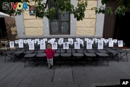 A child stands before a memorial made up of empty chairs bearing images of 43 missing students, set up to mark the nine-month anniversary of their disappearance, in Mexico City, June 27, 2015. 