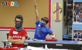 In this July 14, 2020, file photo, amid concerns of the spread of COVID-19, Aiden Trabucco, right, wears a mask as he raises his hand to answer a question behind Anthony Gonzales during a summer STEM camp at Wylie High School in Wylie, Texas.