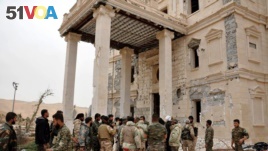 In this photo released on March 24, 2016, by the Syrian official news agency SANA, Syrian government soldiers gather outside a damaged palace, in Palmyra, central Syria.