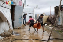 Hassan Fahd al Raja, holding a bucket, helps his siblings drain water out of their family's tent, which is part of a refugee camp in Lebanon's Bekaa valley. (Photo: John Owens for VOA)