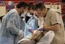 This November 14, 2009 photo shows Dr. Bill Collins, right, working on patient Mendy Johnson as University of Louisville student volunteers Emily Harding, center and Farzan Pouranfar watch during a clinic held by Remote Area Medical.