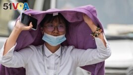 A woman uses a sweater to shield from the sun as she wals on a street on a hot day in Beijing, Monday, July 3, 2023. (AP Photo/Andy Wong)