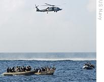 Alleged Somali pirates in the Gulf of Aden raise their hands as US Navy teams in inflatable boats approach and a Navy helicopter patrols overhead, 12 Feb 2009