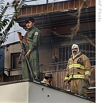 An Afghan policeman stands guard as firefighters are seen in the back ground as the site of an attack in Kabul, Afghanistan, 28 Oct 2009