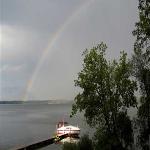 A boat sits near a dock on the western side of Cayuga Lake as a rainbow shines over the opposite shore