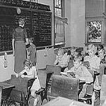 In this photo of an old, one-room classroom in Grundy, Iowa, the 7-year-old boy getting help at the blackboard is the only second-grader in the class.